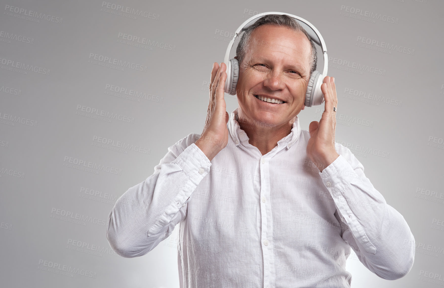 Buy stock photo Shot of a handsome mature businessman standing against a grey background in the studio and listening to music through headphones