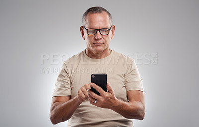 Buy stock photo Shot of a handsome mature man standing alone against a grey background in the studio and using his cellphone