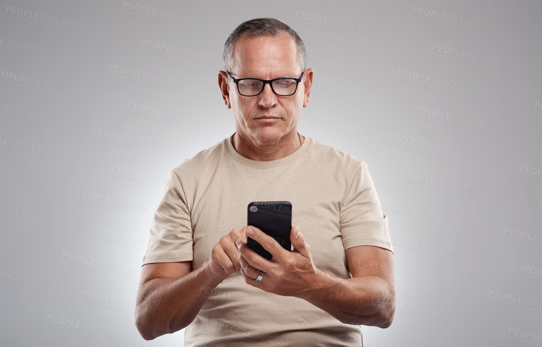 Buy stock photo Shot of a handsome mature man standing alone against a grey background in the studio and using his cellphone