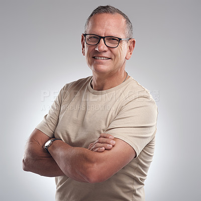 Buy stock photo Shot of a handsome mature man standing alone against a grey background in the studio with his arms folded