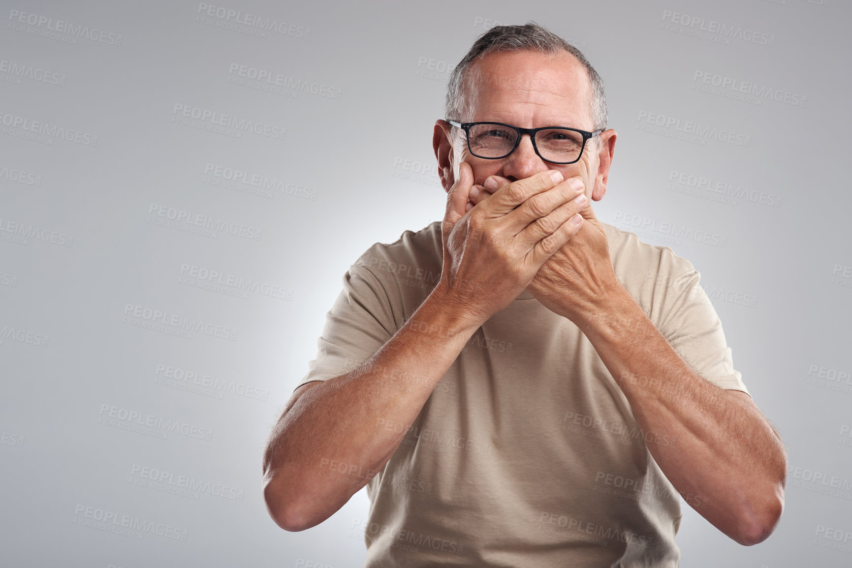 Buy stock photo Shot of a mature man standing against a grey background in the studio and covering his mouth with his hands