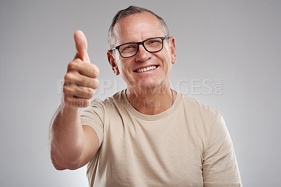 Buy stock photo Shot of a handsome mature man standing against a grey background in the studio and making a thumbs up gesture