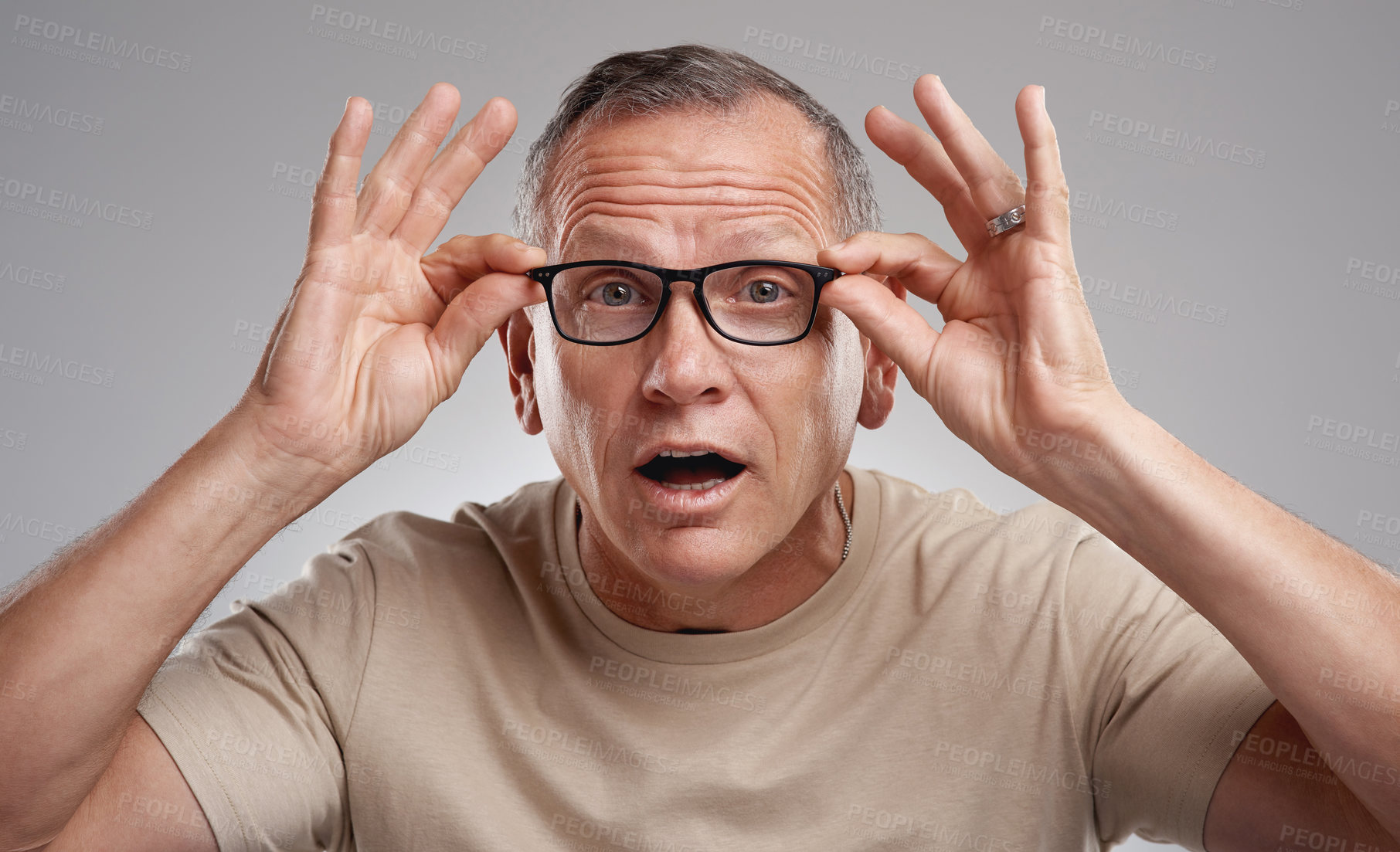 Buy stock photo Shot of a handsome mature man standing alone against a grey background in the studio and adjusting his glasses