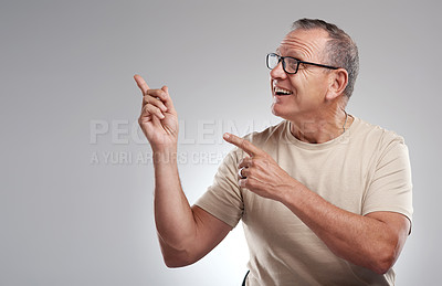 Buy stock photo Shot of a handsome mature man standing alone against a grey background in the studio and pointing at a promotion