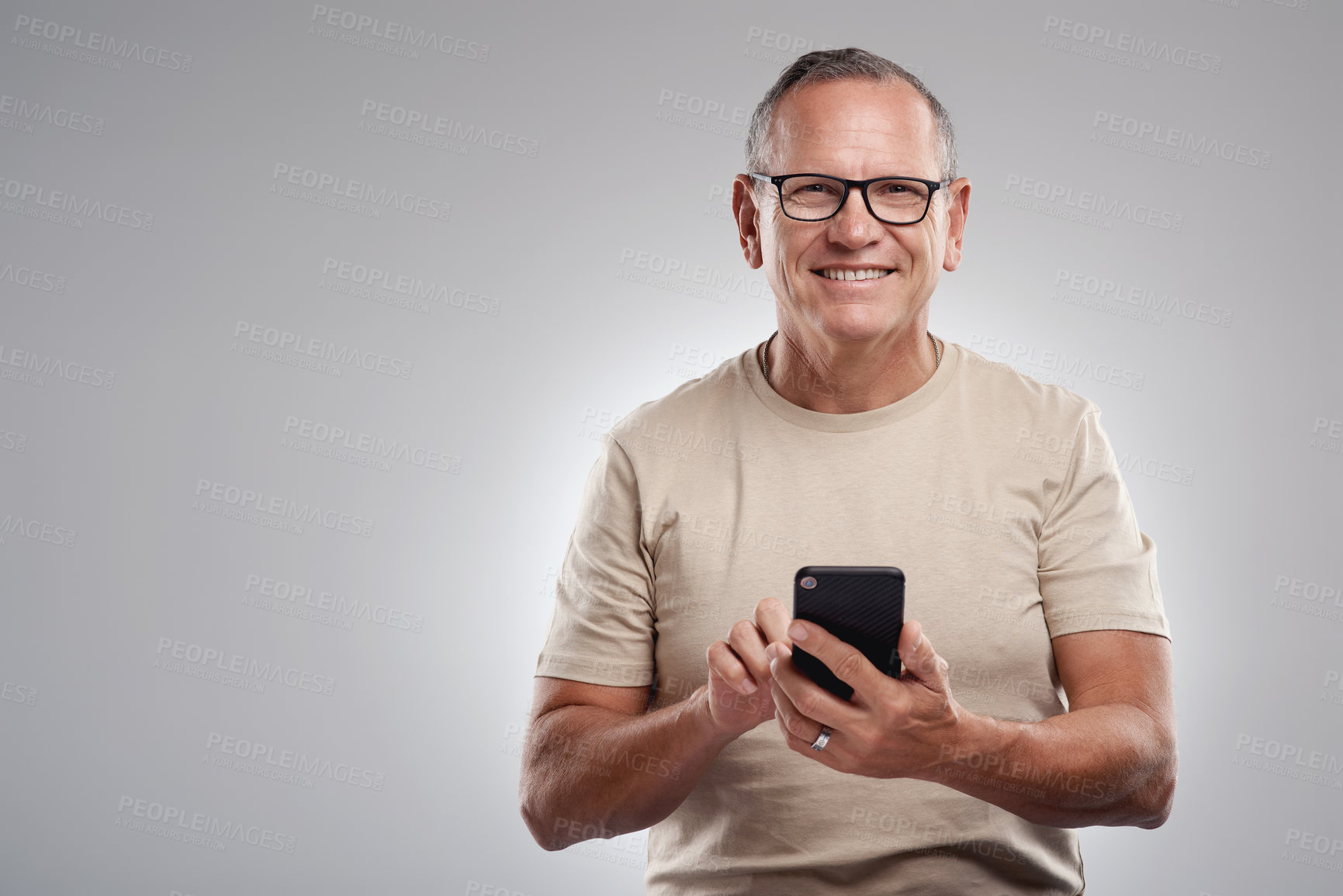 Buy stock photo Shot of a handsome mature man standing alone against a grey background in the studio and using his cellphone