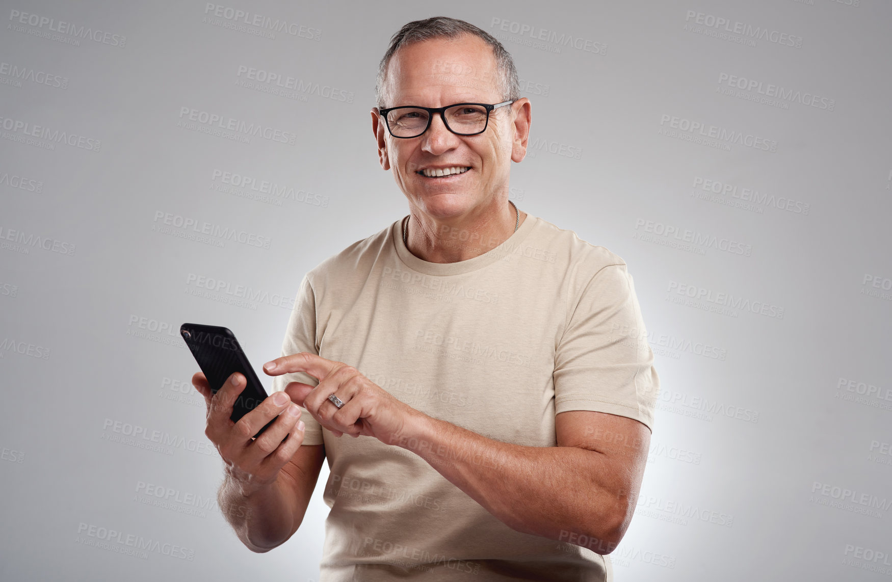 Buy stock photo Shot of a handsome mature man standing alone against a grey background in the studio and using his cellphone