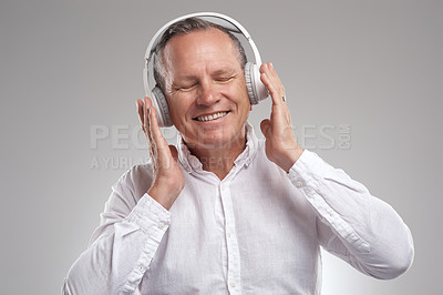 Buy stock photo Shot of a handsome mature businessman standing against a grey background in the studio and listening to music through headphones