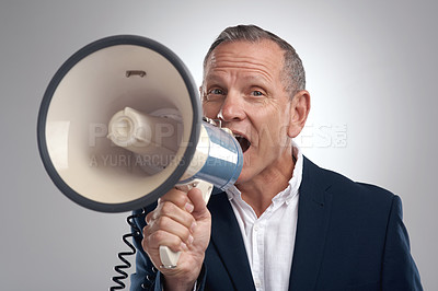 Buy stock photo Shot of a handsome mature businessman standing alone against a grey background in the studio and using a megaphone