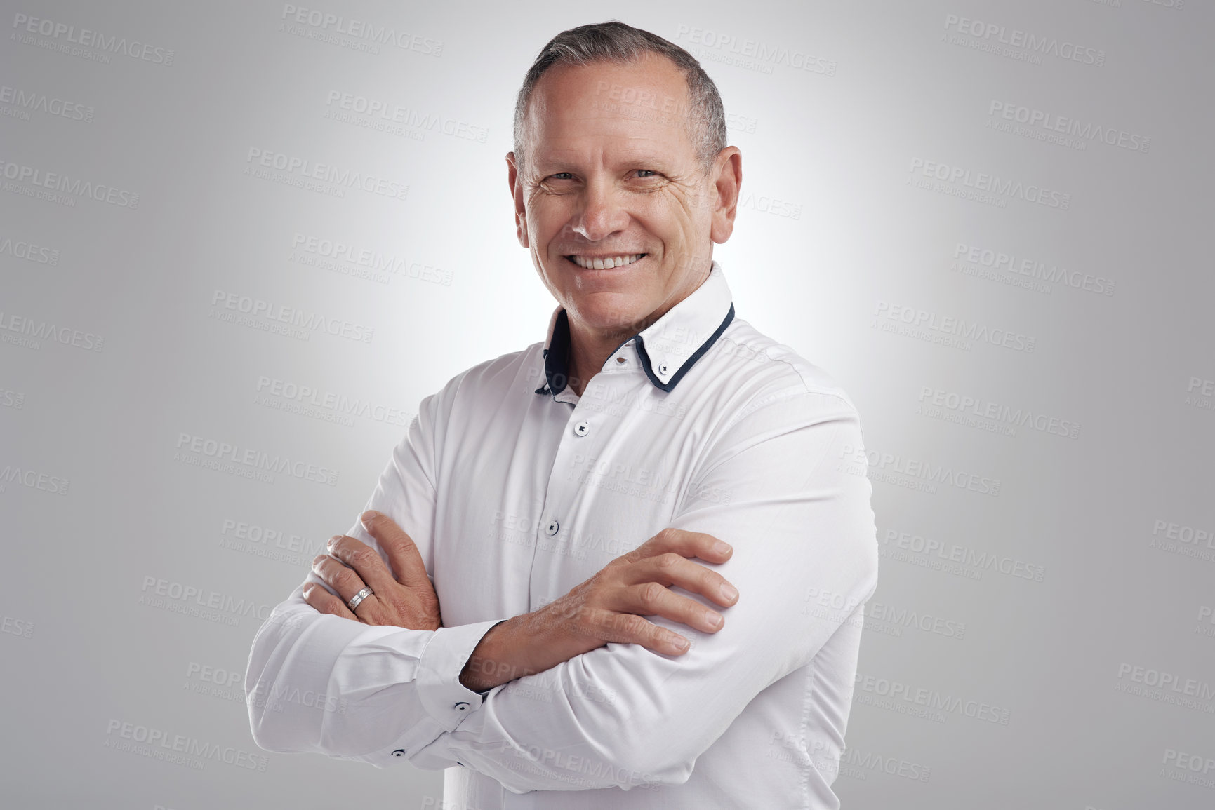 Buy stock photo Shot of a handsome mature businessman standing alone against a grey background in the studio with his arms folded