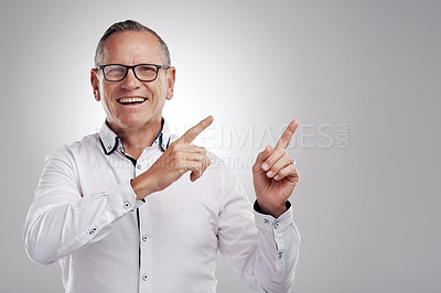 Buy stock photo Shot of a handsome mature businessman standing alone against a grey background in the studio and pointing at a promotion