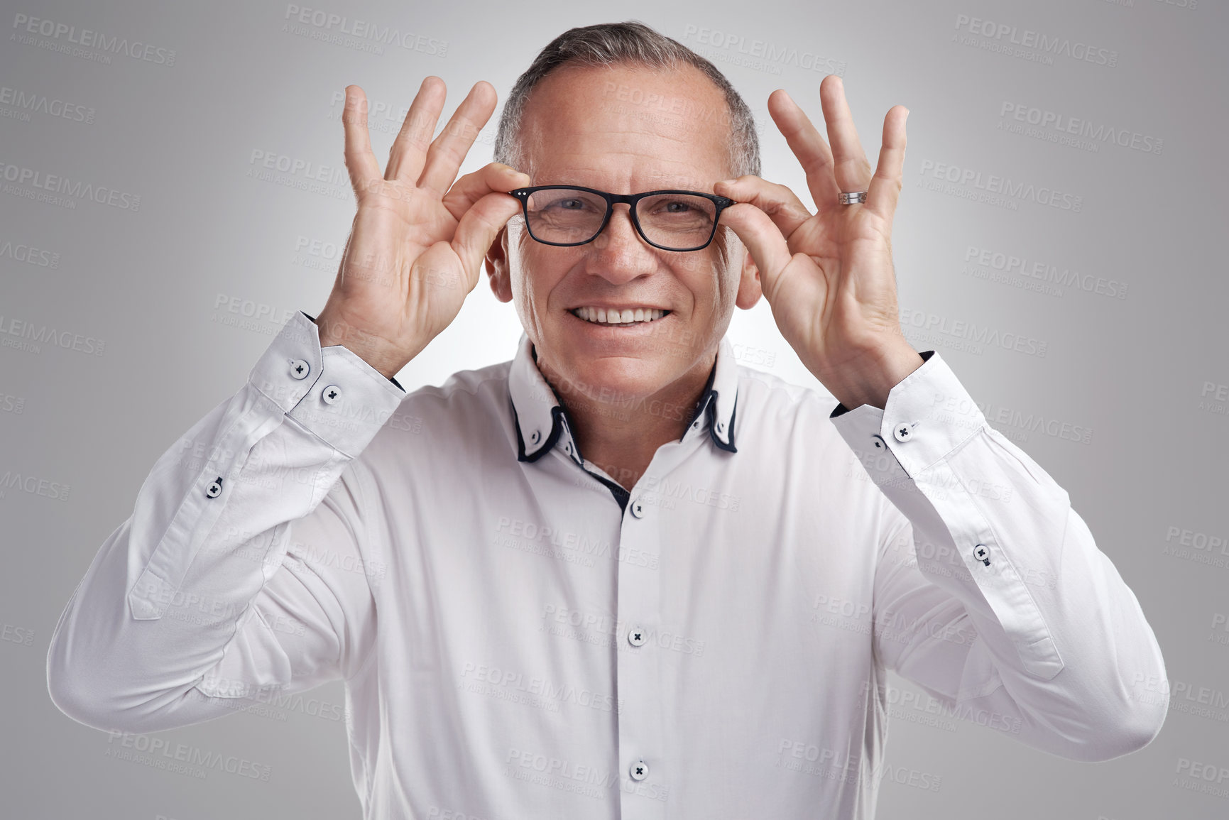 Buy stock photo Shot of a handsome mature businessman standing alone against a grey background in the studio and adjusting his glasses