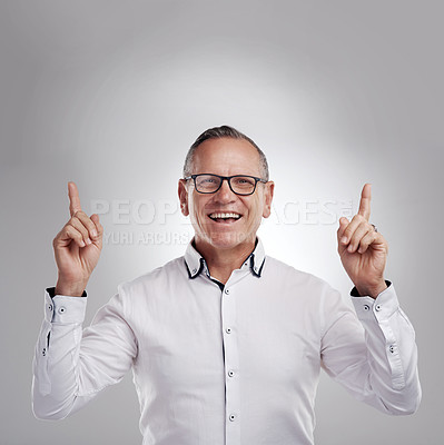 Buy stock photo Shot of a handsome mature businessman standing alone against a grey background in the studio and pointing at a promotion