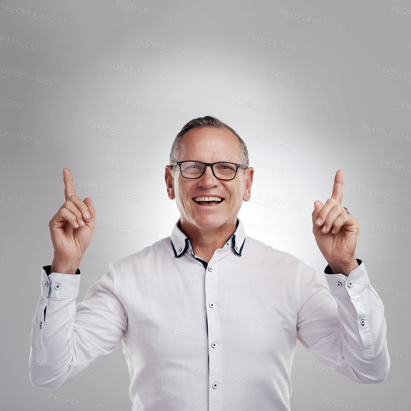 Buy stock photo Shot of a handsome mature businessman standing alone against a grey background in the studio and pointing at a promotion