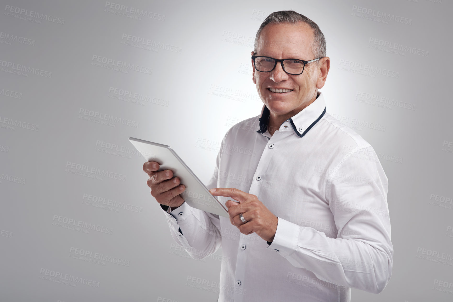Buy stock photo Shot of a handsome mature businessman standing alone against a grey background in the studio and using a digital tablet