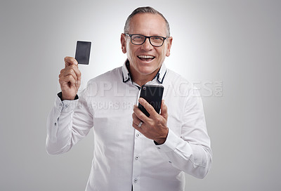 Buy stock photo Shot of a handsome mature businessman standing against a grey studio background and using his cellphone for online shopping