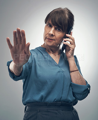 Buy stock photo Studio portrait of a mature woman gesturing to stop while talking on a cellphone against a grey background