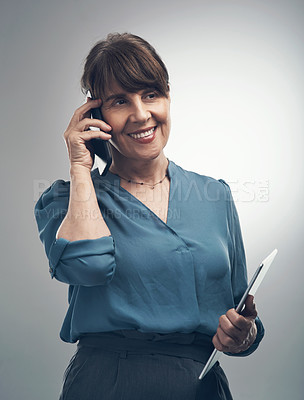 Buy stock photo Studio shot of a senior woman talking on a cellphone while holding a digital tablet against a grey background