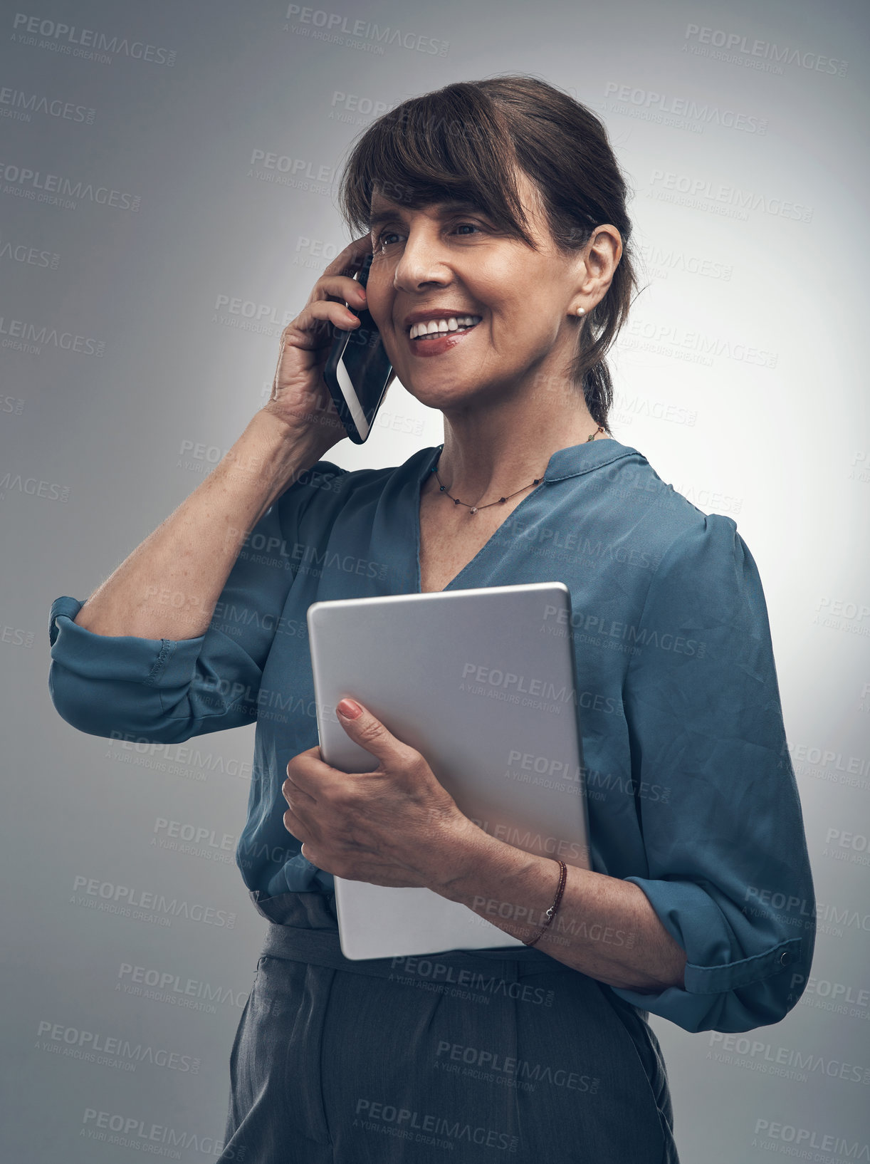 Buy stock photo Studio shot of a senior woman talking on a cellphone while holding a digital tablet against a grey background
