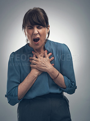 Buy stock photo Studio shot of a senior woman holding her chest in pain against a grey background