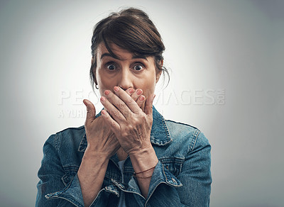 Buy stock photo Studio portrait of a senior woman covering her mouth and looking shocked against a grey background
