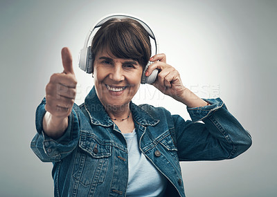 Buy stock photo Studio portrait of a senior woman showing thumbs up while wearing headphones against a grey background