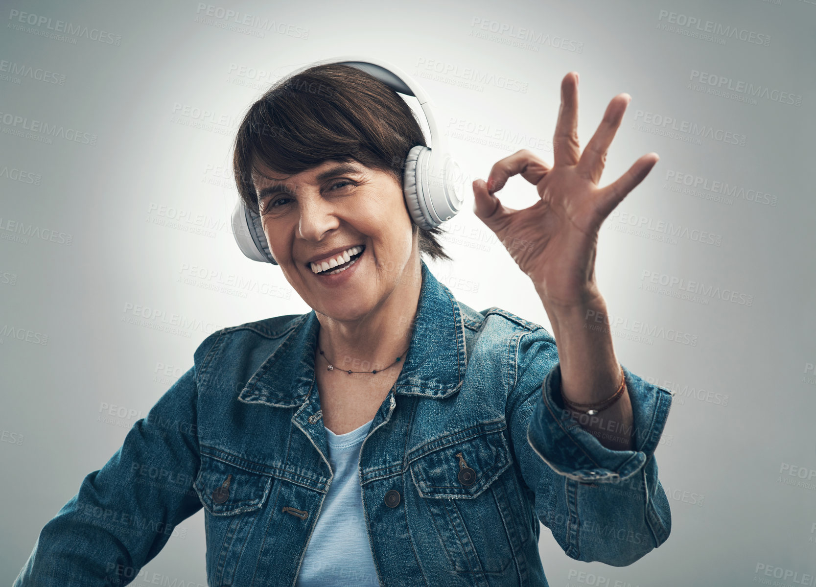 Buy stock photo Studio portrait of a senior woman making an okay gesture while wearing headphones against a grey background