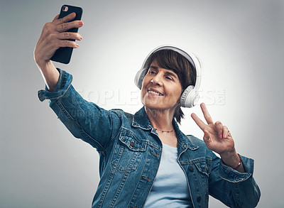 Buy stock photo Studio shot of a senior woman taking selfies while wearing headphones against a grey background