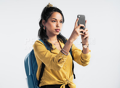 Buy stock photo Shot of a young woman wearing a backpack and taking pictures on her cellphone