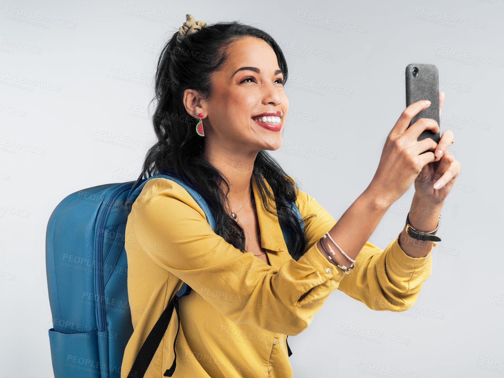 Buy stock photo Shot of a young woman wearing a backpack and taking pictures on her cellphone