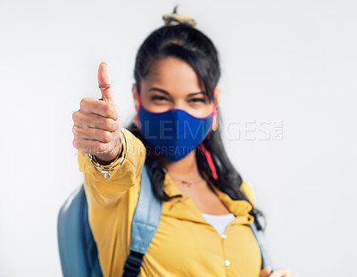 Buy stock photo Studio shot of a young woman showing thumbs up while wearing a mask and a backpack