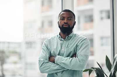 Buy stock photo Shot of a handsome young businessman standing alone in his office with his arms crossed during the day