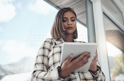 Buy stock photo Shot of an attractive young businesswoman standing alone in her office and using a digital tablet