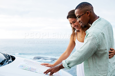 Buy stock photo Shot of a happy young couple reading a map on a road trip along the coast