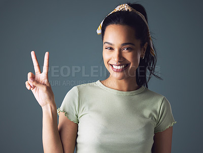 Buy stock photo Studio shot of a young woman showing the peace sign while standing against a grey background