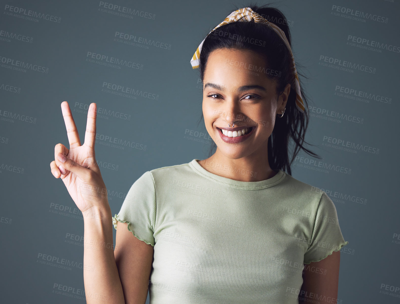 Buy stock photo Studio shot of a young woman showing the peace sign while standing against a grey background