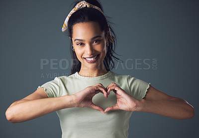 Buy stock photo Studio shot of a young woman forming a heart shape while standing against a grey background
