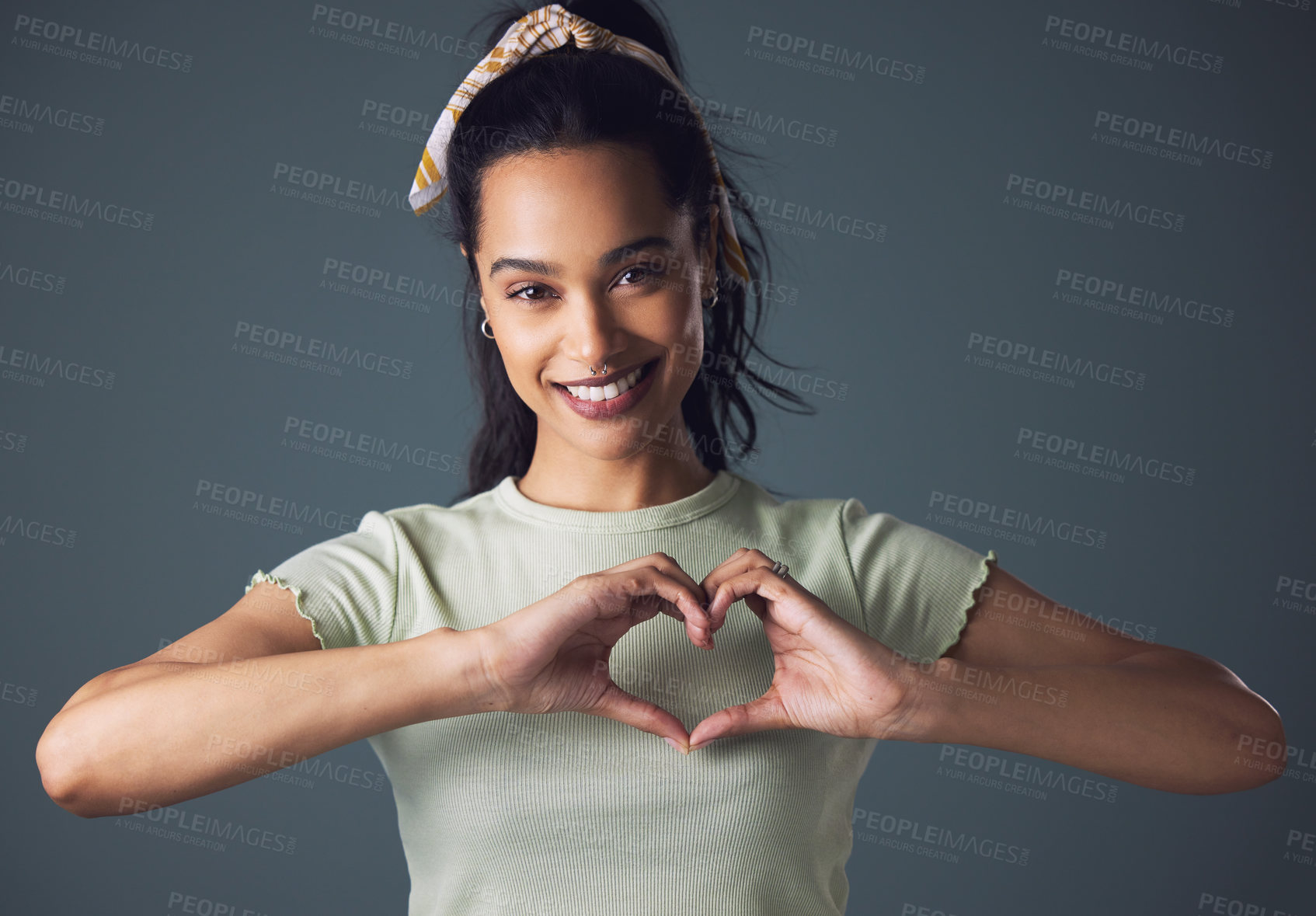 Buy stock photo Studio shot of a young woman forming a heart shape while standing against a grey background