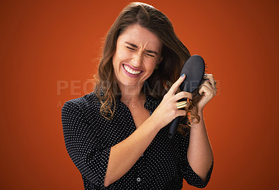 Buy stock photo Shot of an attractive young woman standing against a red background in the studio and struggling to brush her hair