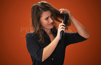 Buy stock photo Shot of an attractive young woman standing against a red background in the studio and struggling to brush her hair