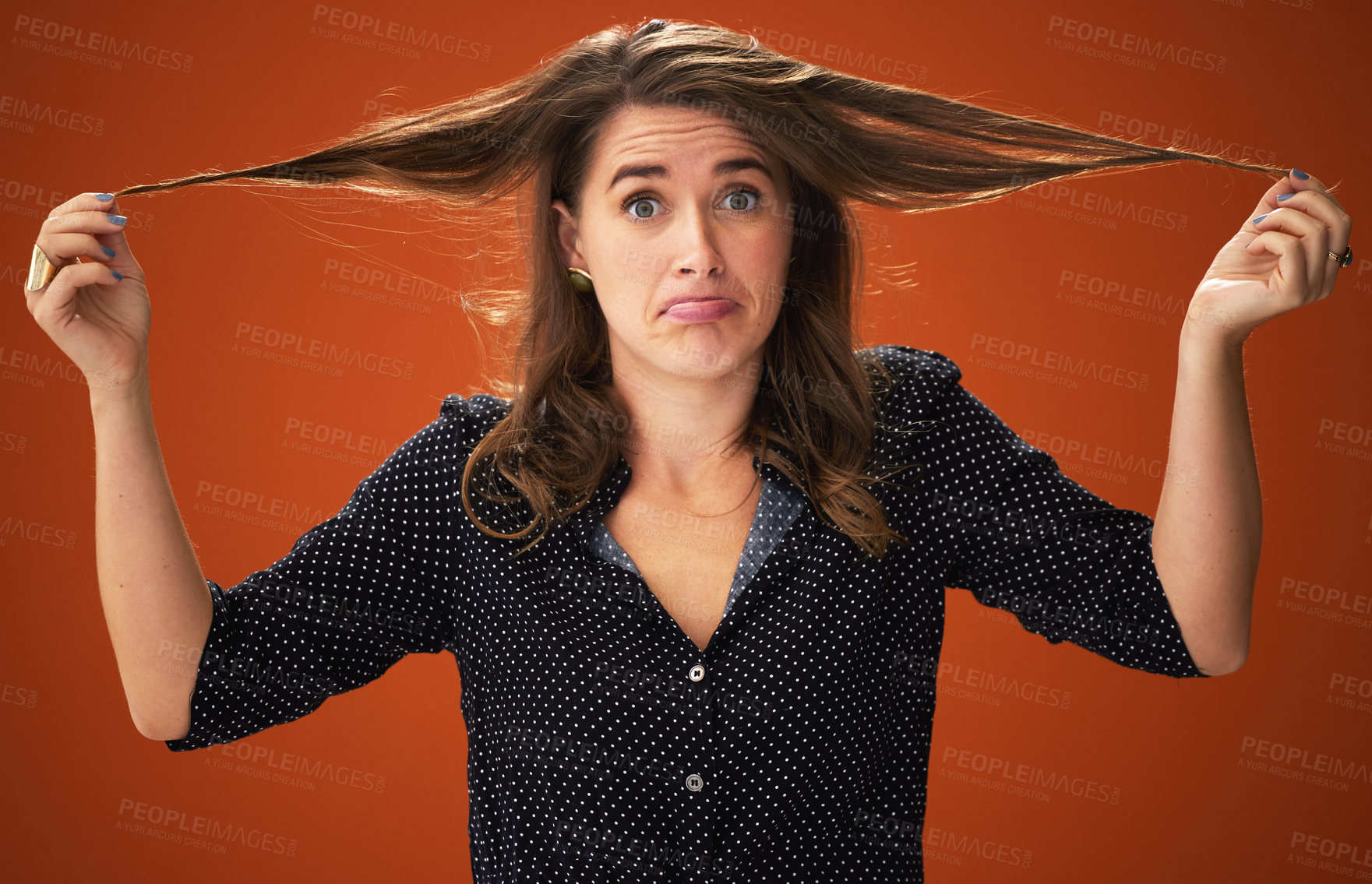 Buy stock photo Shot of an attractive young woman standing alone against a red background in the studio and touching her hair