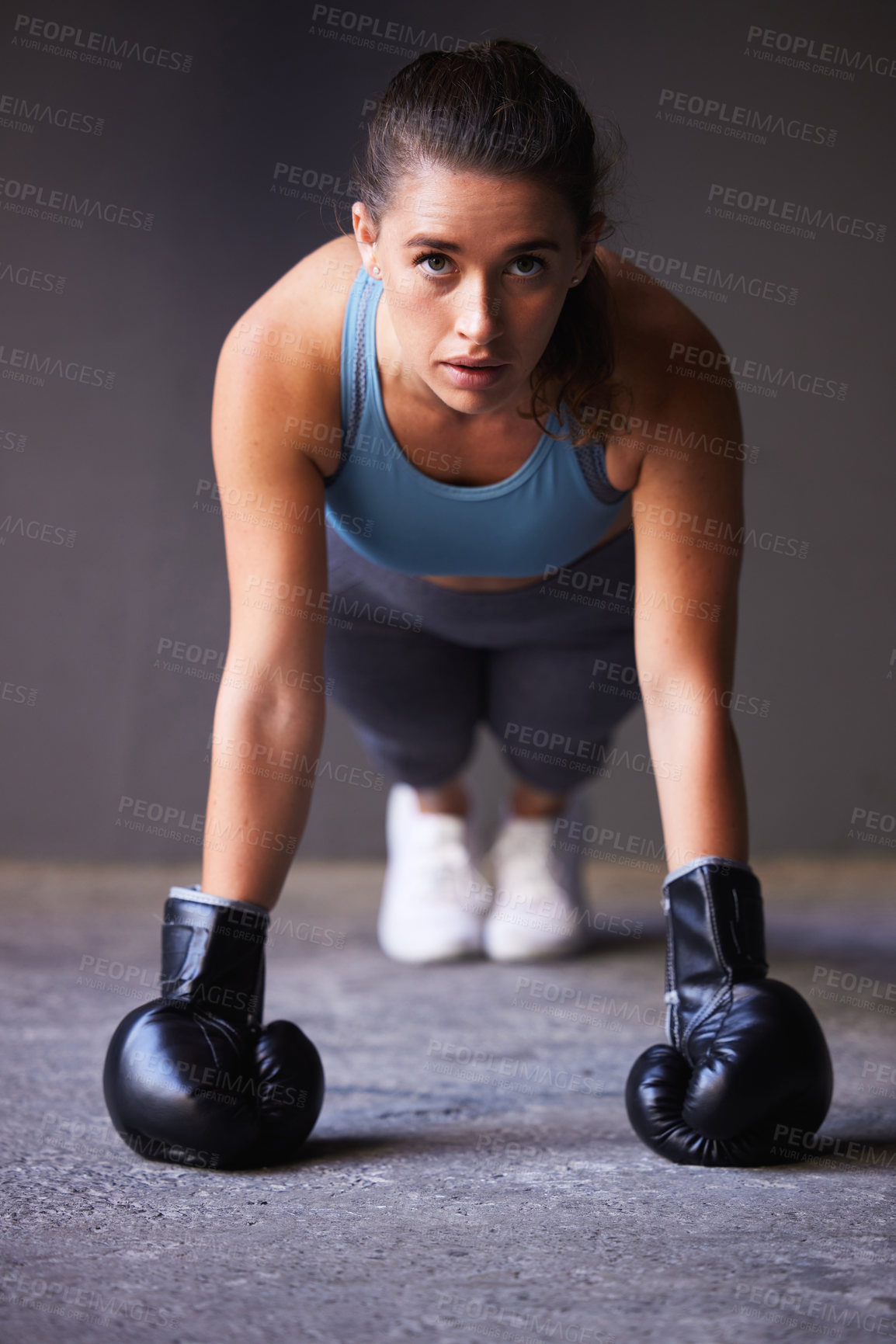 Buy stock photo Portrait of a young woman exercising while wearing boxing gloves