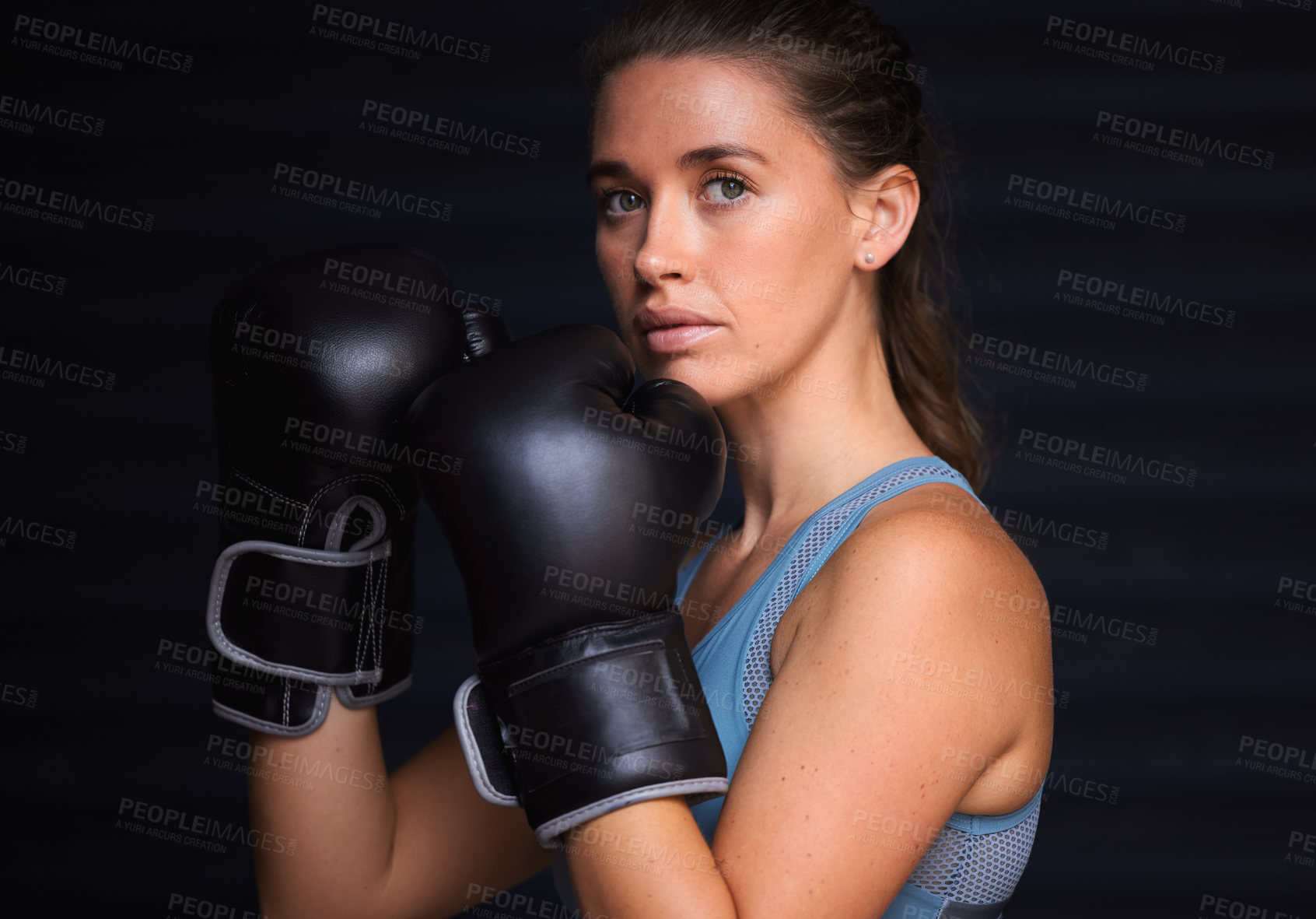 Buy stock photo Portrait of a young woman wearing boxing gloves against a black background