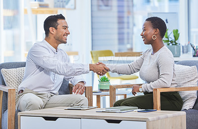 Buy stock photo Shot of two businesspeople shaking hands while sitting together in an office