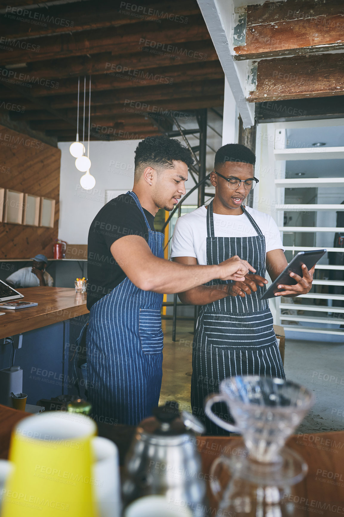 Buy stock photo Shot of two young men using a digital tablet while working in a cafe