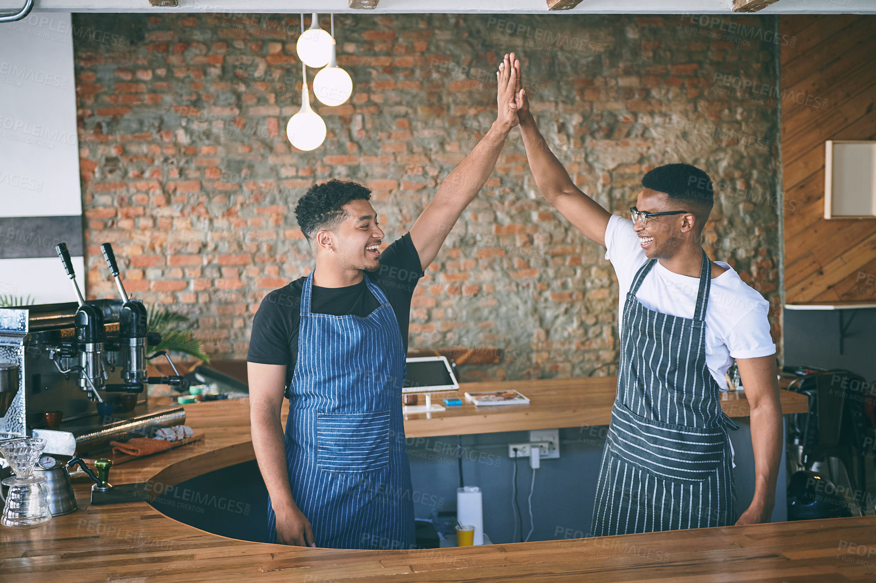 Buy stock photo Shot of two confident young men giving each other a high five while working in a cafe