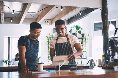 Buy stock photo Shot of two young men using a digital tablet while working in a cafe