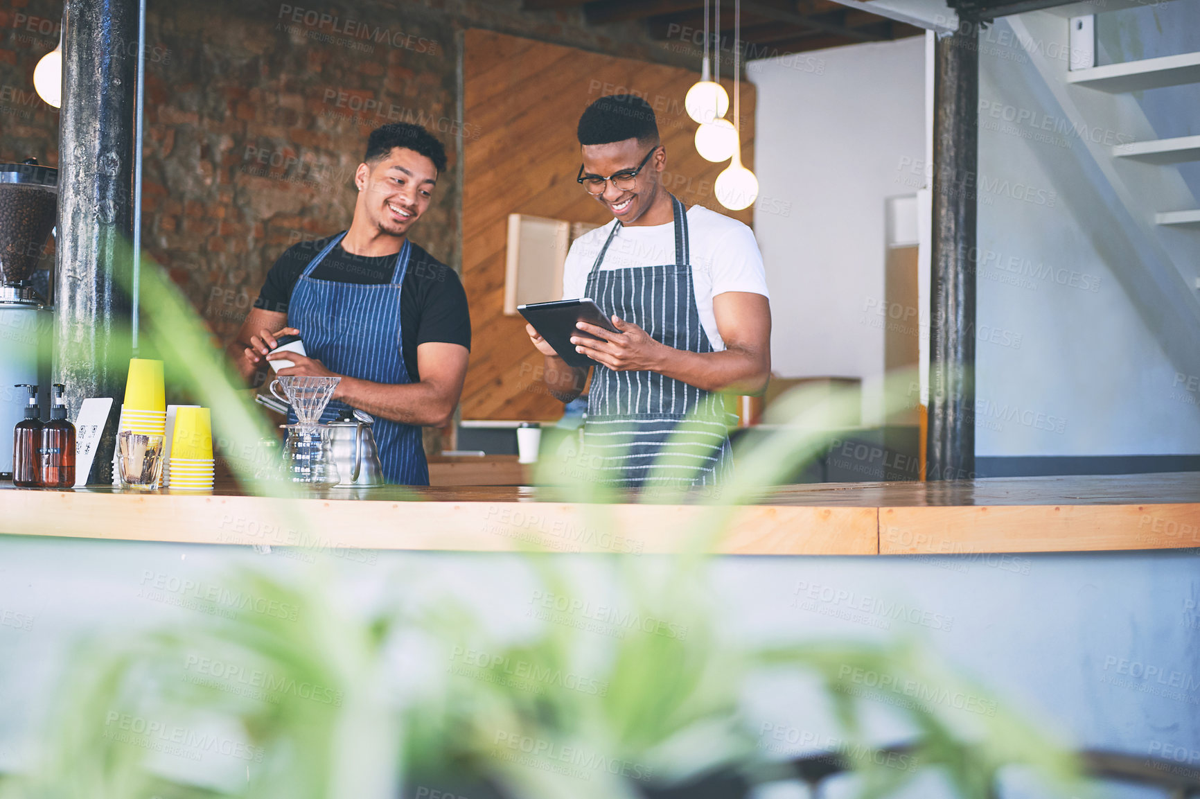 Buy stock photo Shot of two young men using a digital tablet while making coffee at a cafe