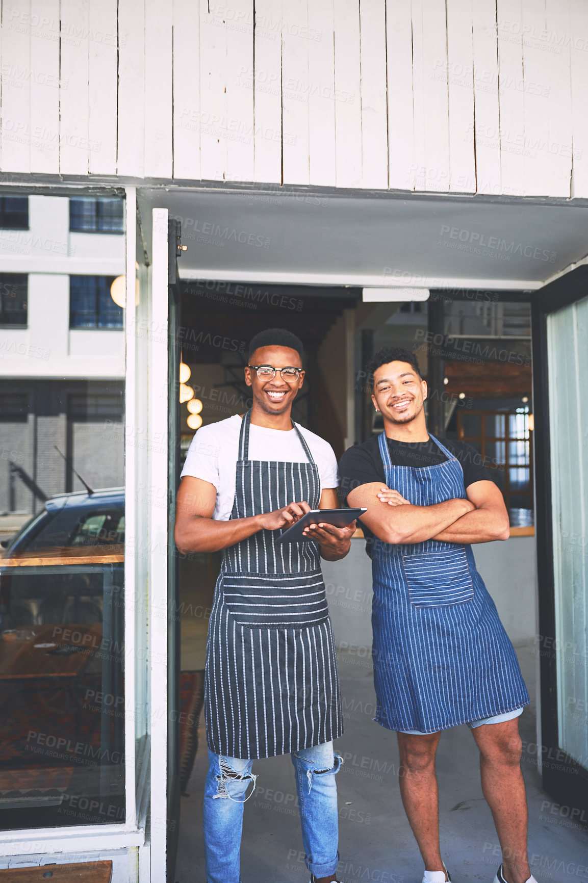 Buy stock photo Shot of two young men using a digital tablet while standing at the entrance of a cafe