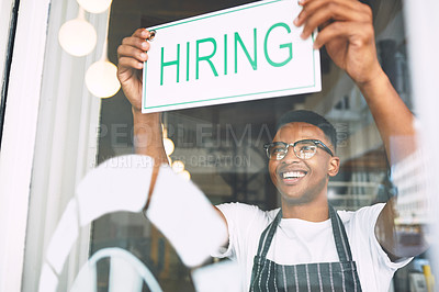 Buy stock photo Shot of a young man hanging up a hiring sign while working in a cafe