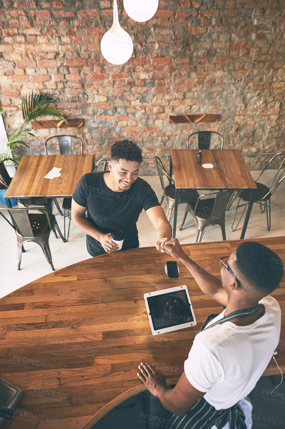 Buy stock photo Shot of a young man serving a customer coffee and giving him a fist bump in a cafe